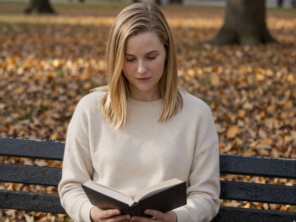 Woman in a cozy sweater reading at a park bench on a fall afternoon